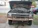 1986 Ford Bronco - Front view of a dark blue Ford Bronco with hood open, revealing the engine compartment and a bull bar.