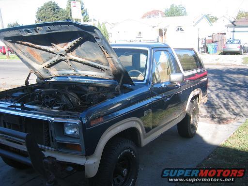Dark blue Ford Bronco with hood open, tan interior, and a chrome bumper