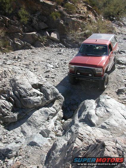 Red SUV navigating a rocky, off-road trail. It has a brush guard and lifted suspension