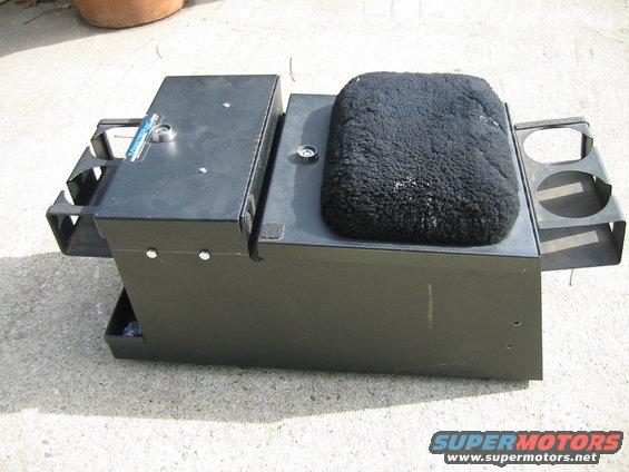 Black metal center console with cup holders and a fuzzy seat, on concrete