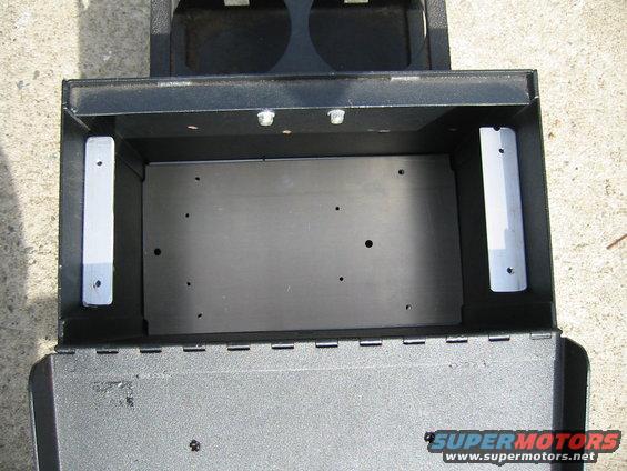 Black center console storage compartment with metal mounting brackets and two circular openings at the top