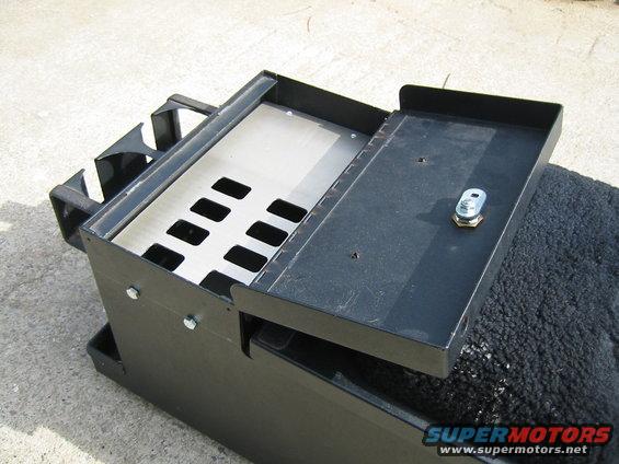 Black metal storage box with lid open, showing compartments and a lock. It sits on a textured surface