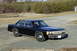 1991 Ford Crown Victoria - This black sedan is parked outdoors on a gravel surface with trees and a fence in the background.