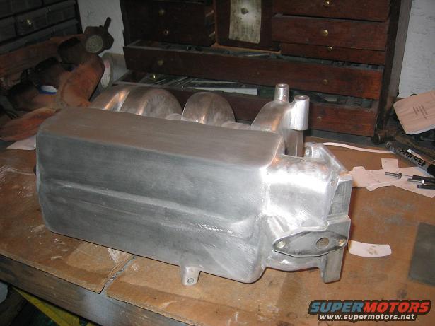 Aluminum intake manifold on a workbench with tools and papers
