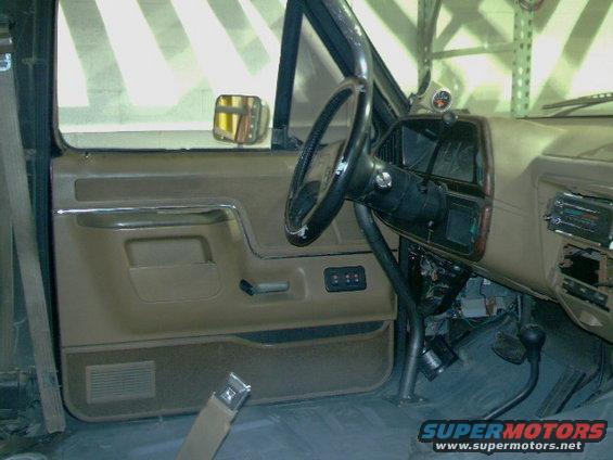Interior view of a truck's driver side door, dashboard, and steering wheel. Roll cage visible