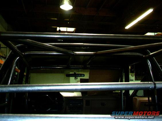 Metal roll cage structure inside a dark vehicle interior, viewed from the rear