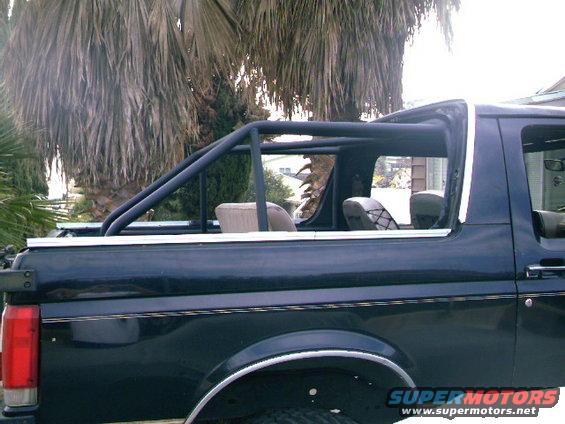 Side view of a dark blue 1989 Ford Bronco with a black roll cage installed in the rear