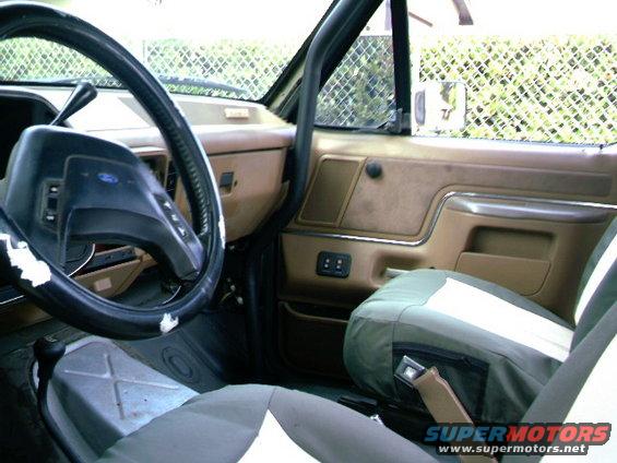 Interior of a vehicle showing the steering wheel, dashboard, door panel, and seat. A roll cage is visible