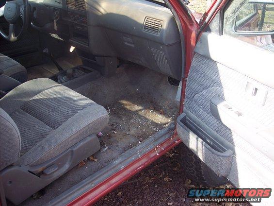Red truck interior with dirty floor, grey fabric seats, and dashboard. The driver's side door is open