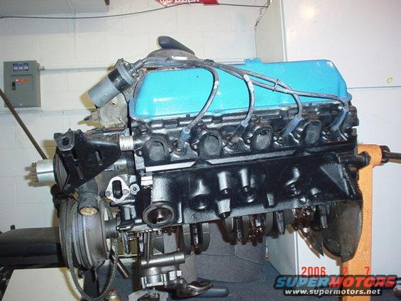 V8 engine with blue valve covers on an engine stand, showing spark plug wires and exhaust manifolds