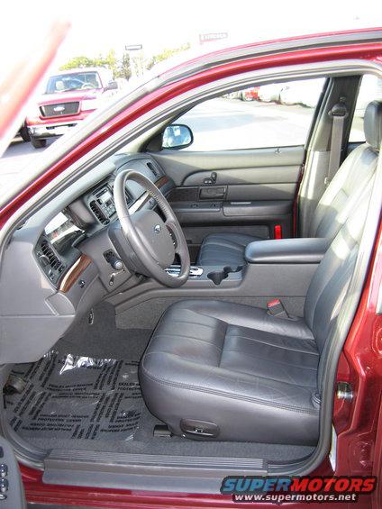 Interior of a 2005 Ford Crown Victoria showing leather seats, dashboard, and steering wheel. A red Ford truck is visible outside