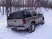 2000 Chevrolet Tahoe - A silver Chevrolet Suburban navigates a snowy path, its tires equipped with snow chains for traction.