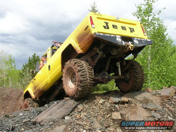 Yellow Jeep Comanche climbing rocky terrain. Driver visible. Some mud on body
