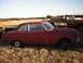 1963 Ford Falcon - A red sedan sits in a field next to a pickup truck, under a clear sky.