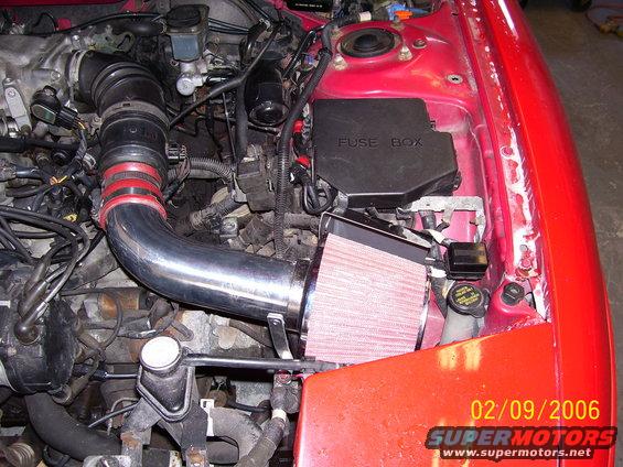 Engine bay showing custom intake piping and red air filter. Fuse box labeled