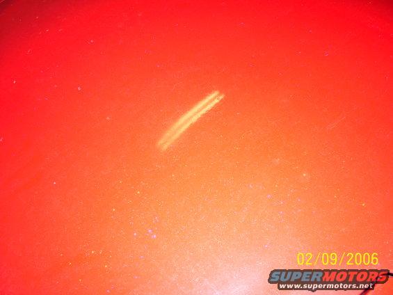 Orange car paint surface with a faint scratch and date stamp 02/09/2006