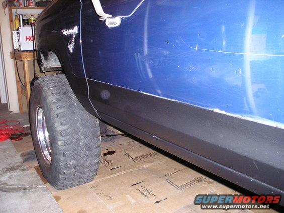 Side view of a blue vehicle's fender, door, and large off-road tire