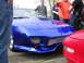 1996 Ford Probe - A group of people gathered around a bright blue sports car, with another red car parked nearby.