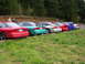 1996 Ford Probe - A line of Ford Probes, including a red 1996 model, are parked in a row next to a wooded area.