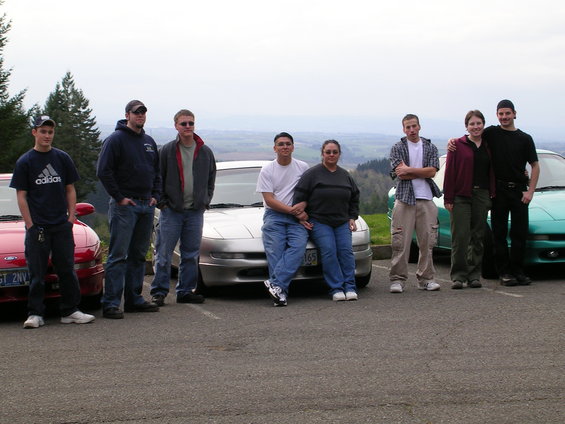 1996 Ford Probe and two other cars with a group of people standing and sitting around them