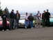 1996 Ford Probe - A group of people gathered around three cars, including a 1996 Ford Probe, outdoors with a scenic view.
