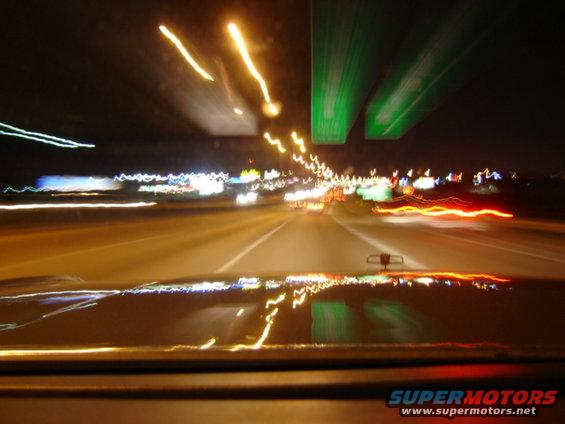 Dashboard view of highway lights at night with a reflection on the hood