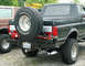 1988 Ford Bronco - Rear view of a dark green Ford Bronco with a spare tire and custom bumper, alongside another vehicle.