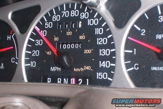 Car dashboard showing odometer at 100,000 miles, speedometer needle near 35 mph, and tachometer needle near 1000 RPM