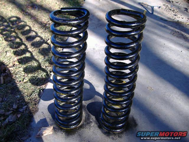 Two black coil springs with yellow bands on a concrete surface