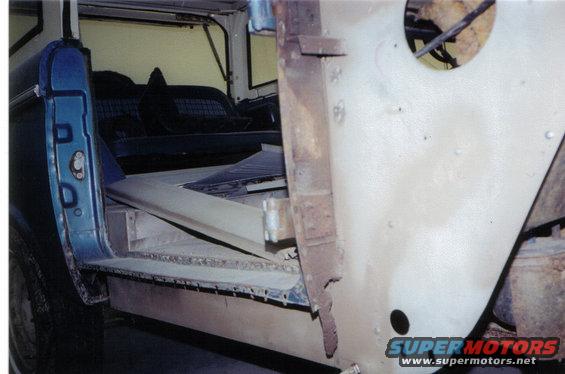 Interior of a blue Ford Bronco showing the driver's side door opening, seats, and a partially disassembled passenger side body panel