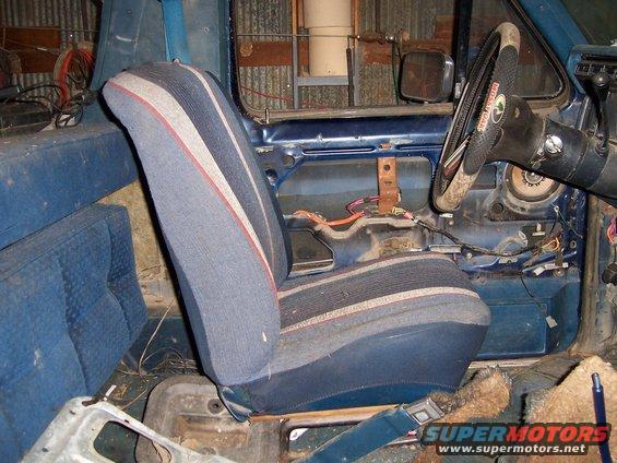 Interior of a blue vehicle with striped seats, exposed wiring, and a steering wheel