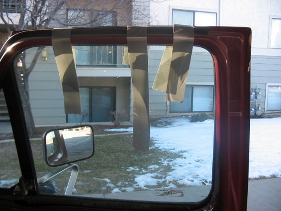 Red car door frame with tape strips across the top of the window opening. Side mirror visible