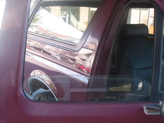 Maroon SUV interior with dark seats visible through the window, reflection of another vehicle on the side window