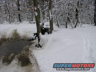 Black all-terrain vehicle partially buried in snow next to a muddy stream