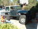 1994 Jeep YJ - A dark green 1994 Jeep YJ with a tan hardtop is parked outside, lifted with large off-road tires.