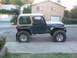 1994 Jeep YJ - A green Jeep Wrangler with a tan soft top is parked on the side of a residential street.
