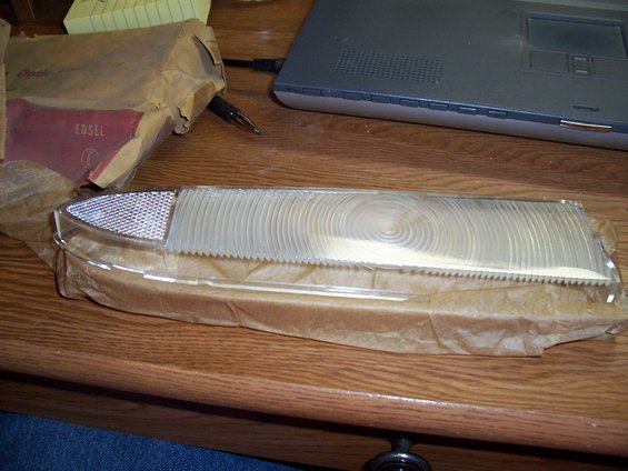 Clear plastic car tail light lens with textured pattern, in brown paper packaging. Text 'EDSEL' visible on packaging