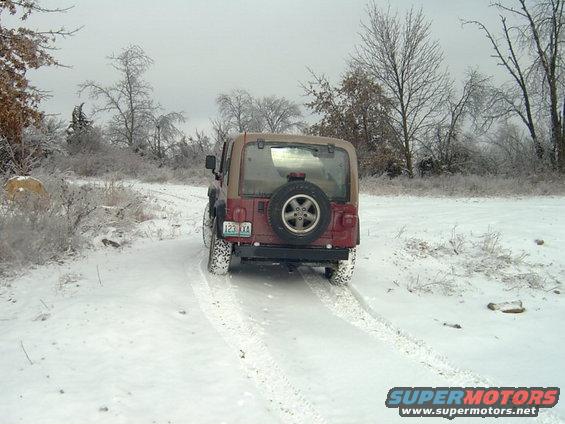 Jeep Wrangler driving on a snowy trail, rear view. License plate reads 123 XXA