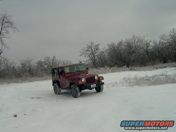 Red Jeep Wrangler in snow, 3/4 front view. License plate visible