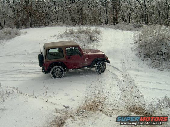 1998 Jeep TJ driving on a snow-covered dirt road with trees in the background