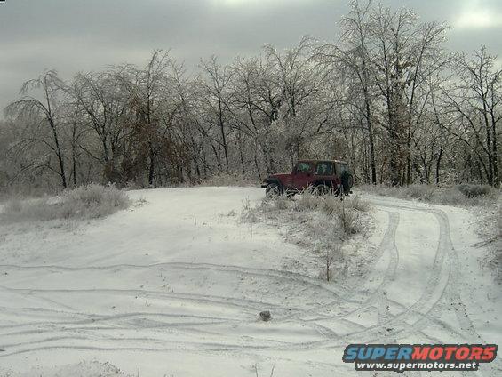 Red Jeep Wrangler on a snowy, icy road with trees covered in ice