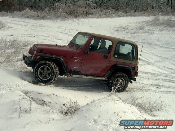 Red Jeep Wrangler driving on a snowy trail. The Jeep has a tan soft top