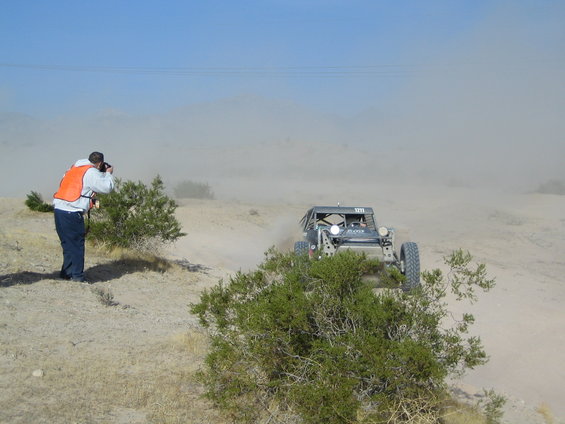 Off-road buggy kicking up dust on a dirt track, photographer in foreground