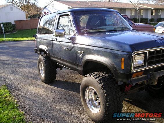Dark blue SUV with lifted suspension, large tires, and chrome wheels. Visible badge on fender