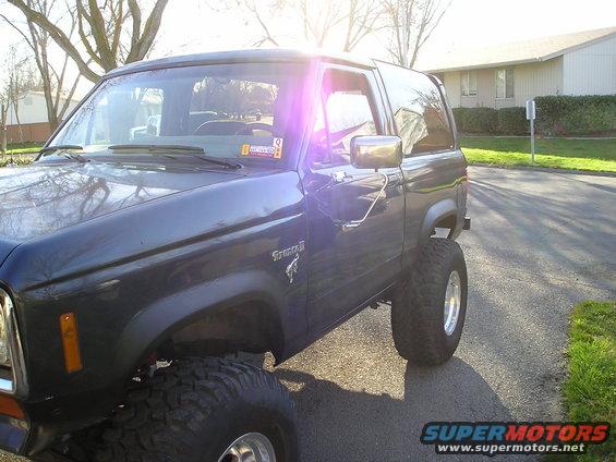 Dark blue Ford Bronco II with lifted suspension and large tires, seen from the front three-quarter angle