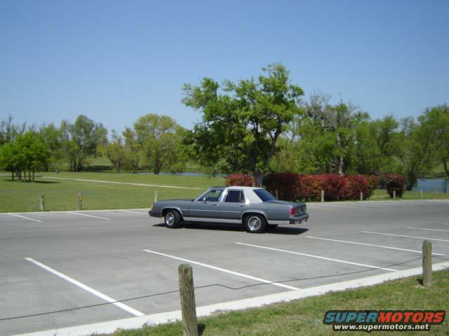 1988 Ford Crown Victoria LTD parked in an empty lot with trees and a body of water in the background