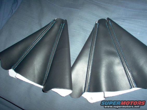 Two black leather shift boot covers with blue stitching, laid flat on a dark surface