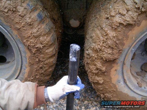 Mud-caked tires of a large vehicle with a gloved hand holding a metal tool between them