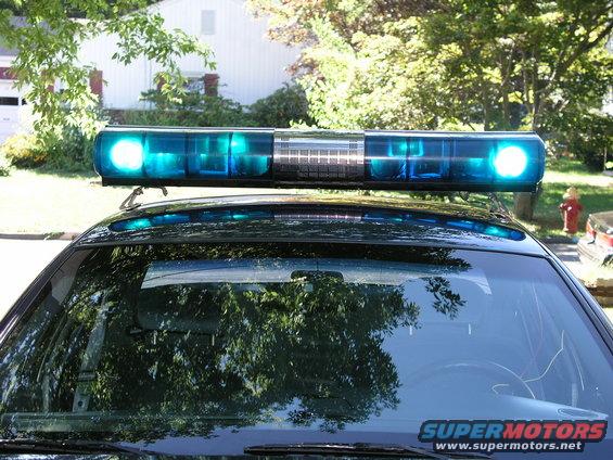 Police car roof with blue light bar. "SUPERMOTORS" text visible on windshield