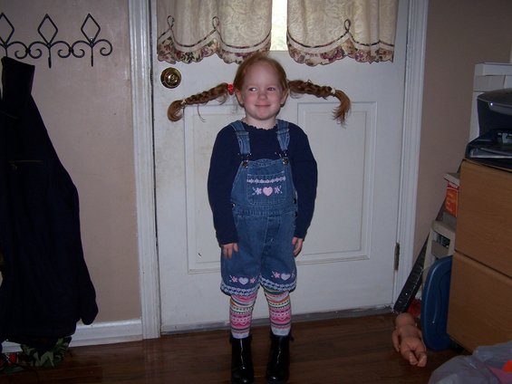 Young girl with pigtails, wearing overalls and colorful socks, stands in front of a door